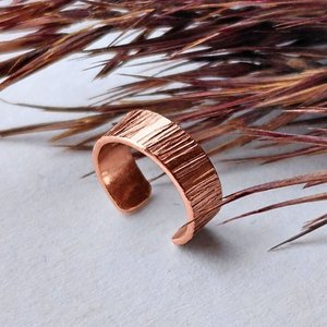 Handmade copper ear cuff with textured surface shown against natural dried grasses