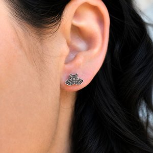 Copper moth stud earring worn on a woman's earlobe, showing the small size and detail
