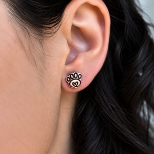 Copper paw print stud earring worn on a woman's earlobe, showing the petite size and heart detail