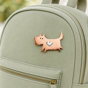 Copper scruffy terrier dog pin brooch with a silver heart, attached to a sage green backpack