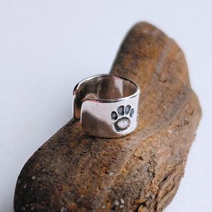 Sterling silver paw print helix cuff shown from an angled view on a piece of natural driftwood