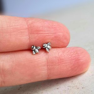 Tiny 5mm fine silver bee stud earrings shown on fingertips for scale, with sterling silver posts and butterfly backs