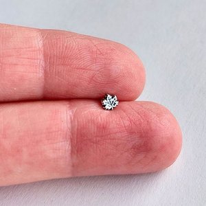 Tiny fine silver maple leaf nose stud shown between fingertips to illustrate its petite size