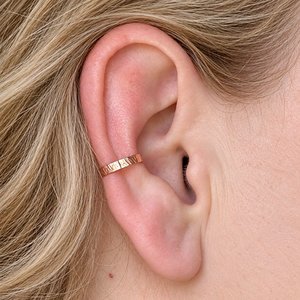 Hammered copper ear cuff shown being worn on the conch of a fair-haired woman's ear
