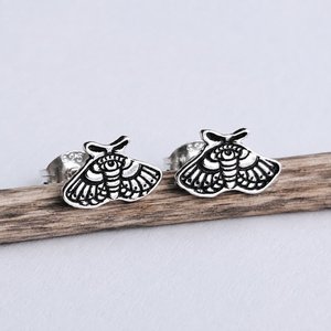 Pair of handmade sterling silver moth stud earrings displayed on natural wood