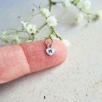 Personalised sterling silver heart charm with hand stamped initial shown on a fingertip for scale