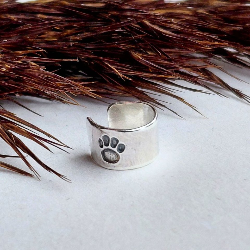 Sterling silver paw print helix cuff shown on a white background with dried grasses