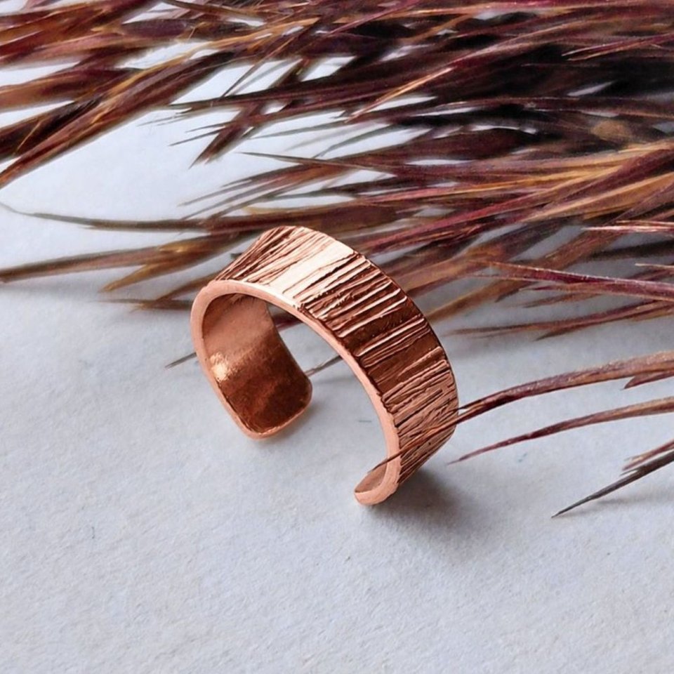 Handmade copper ear cuff with textured surface shown against natural dried grasses