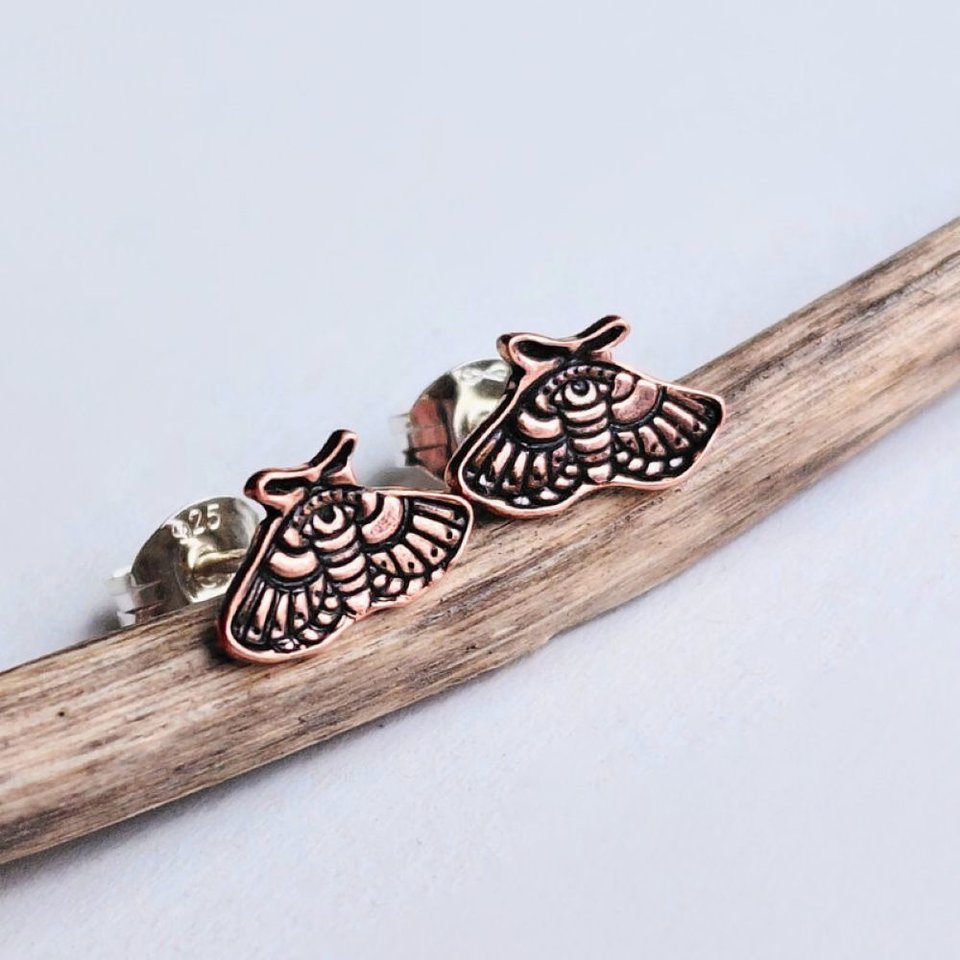 Copper moth stud earrings shown at an angle, highlighting the detailed cut-out moth design