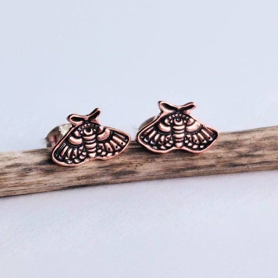 Pair of copper moth stud earrings displayed side by side on natural wood
