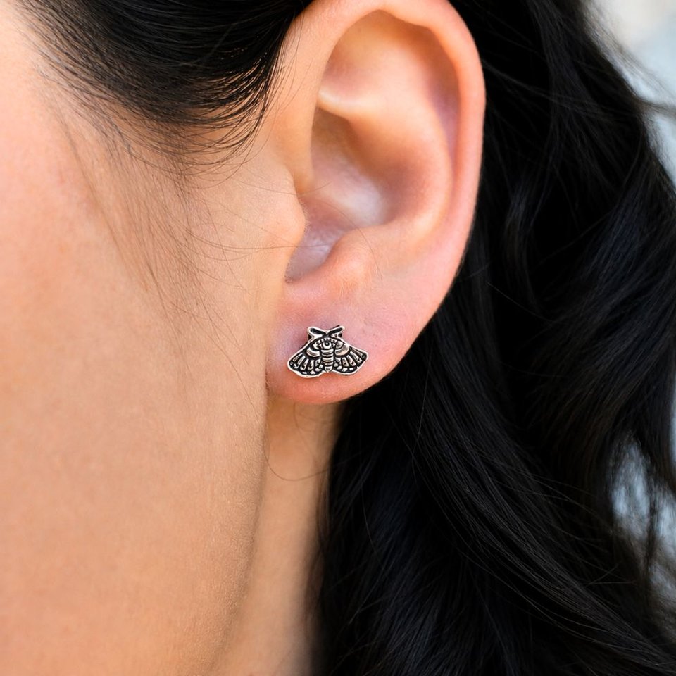 Copper moth stud earring worn on a woman's earlobe, showing the small size and detail