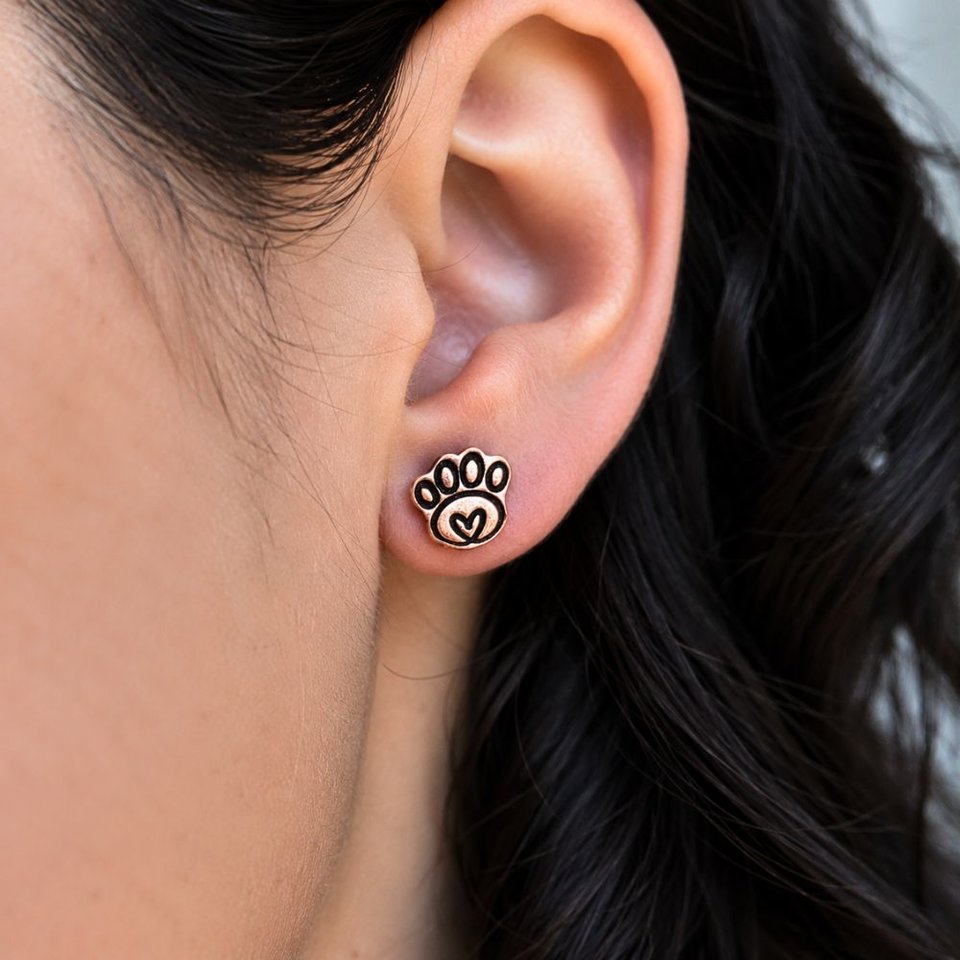 Copper paw print stud earring worn on a woman's earlobe, showing the petite size and heart detail