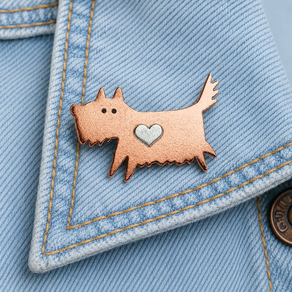 Copper scruffy terrier dog pin brooch with a silver heart, attached to a pale blue denim jacket lapel
