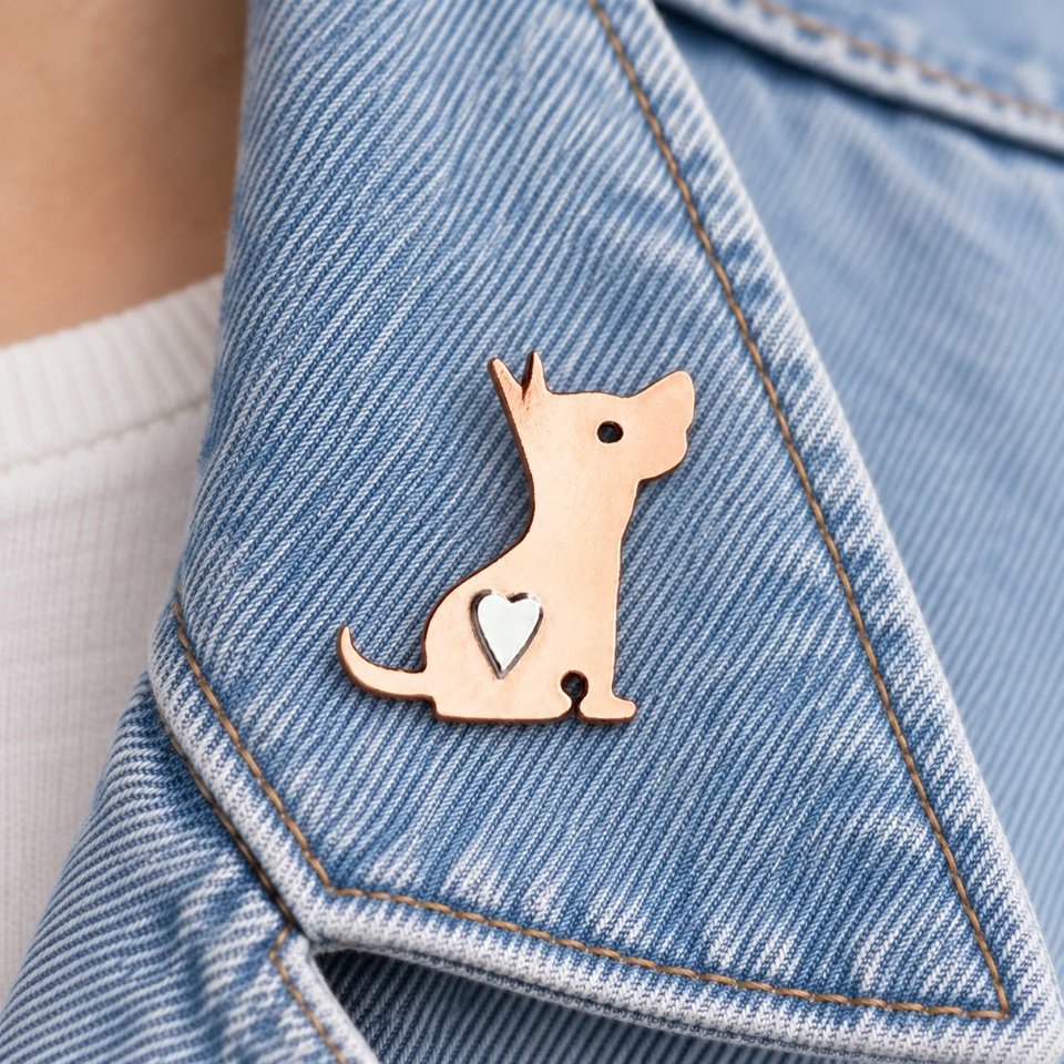 Copper terrier dog pin brooch with a silver heart, attached to a pale blue denim jacket lapel