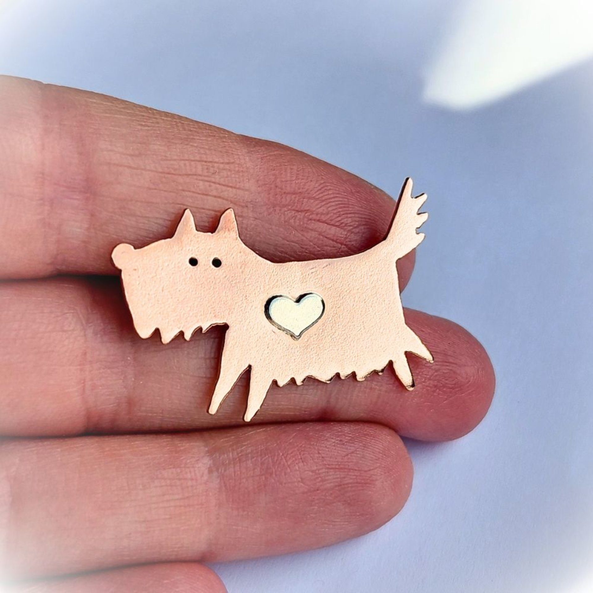 Copper scruffy terrier dog brooch shown in a hand to illustrate its size