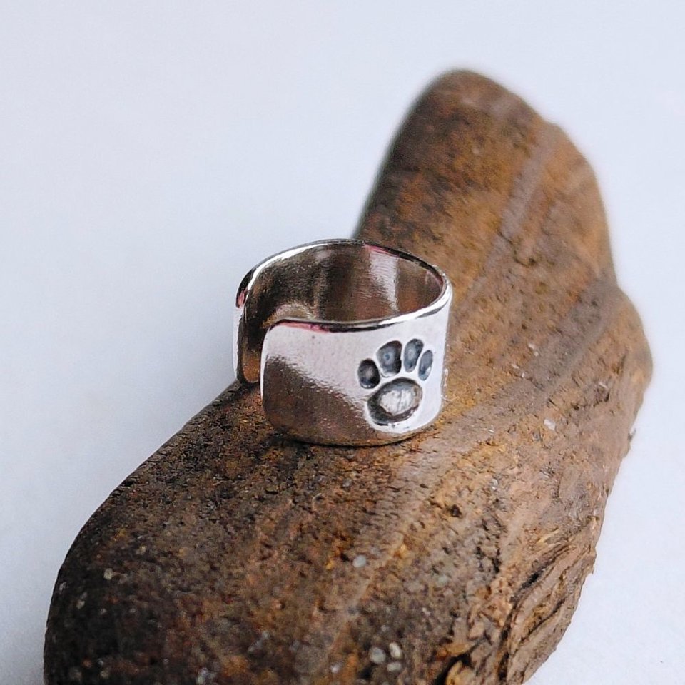 Sterling silver paw print helix cuff shown from an angled view on a piece of natural driftwood