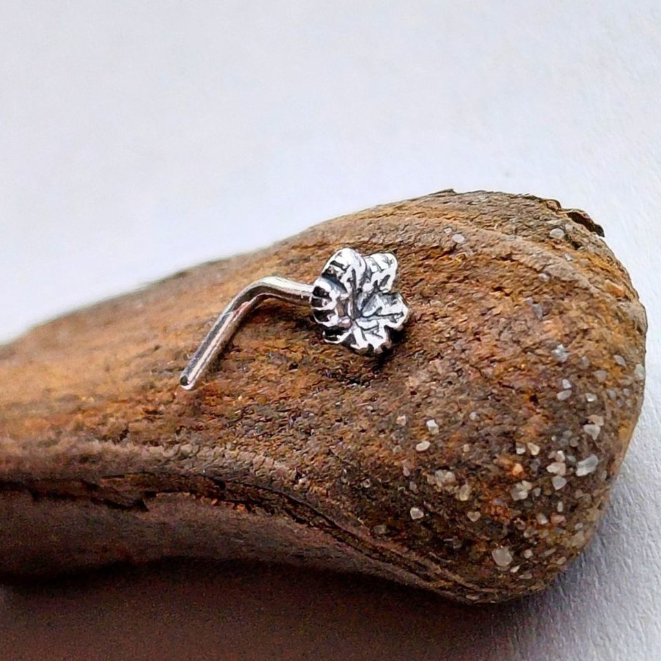 Handcrafted fine silver maple leaf nose stud with sterling silver L-shaped post, shown on natural wood