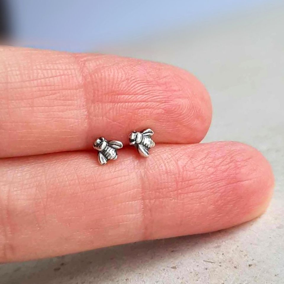 Tiny 5mm fine silver bee stud earrings shown on fingertips for scale, with sterling silver posts and butterfly backs
