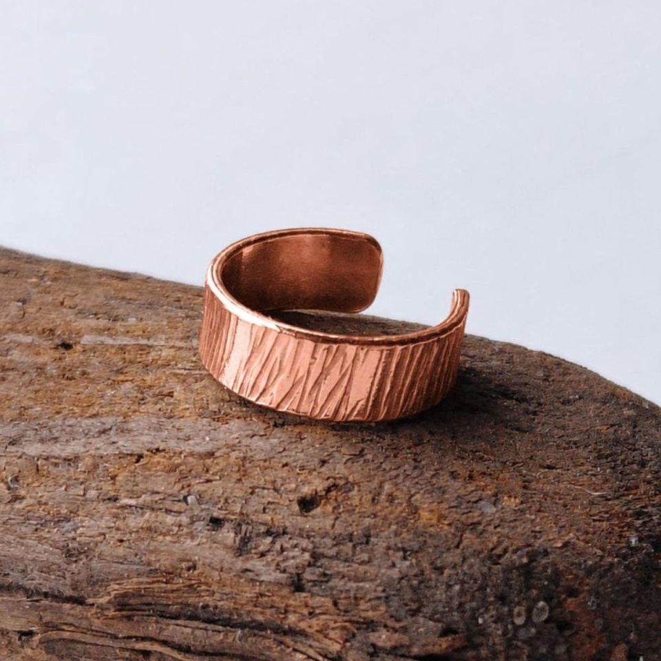 Hammered copper ear cuff with organic textured finish displayed on rustic wood