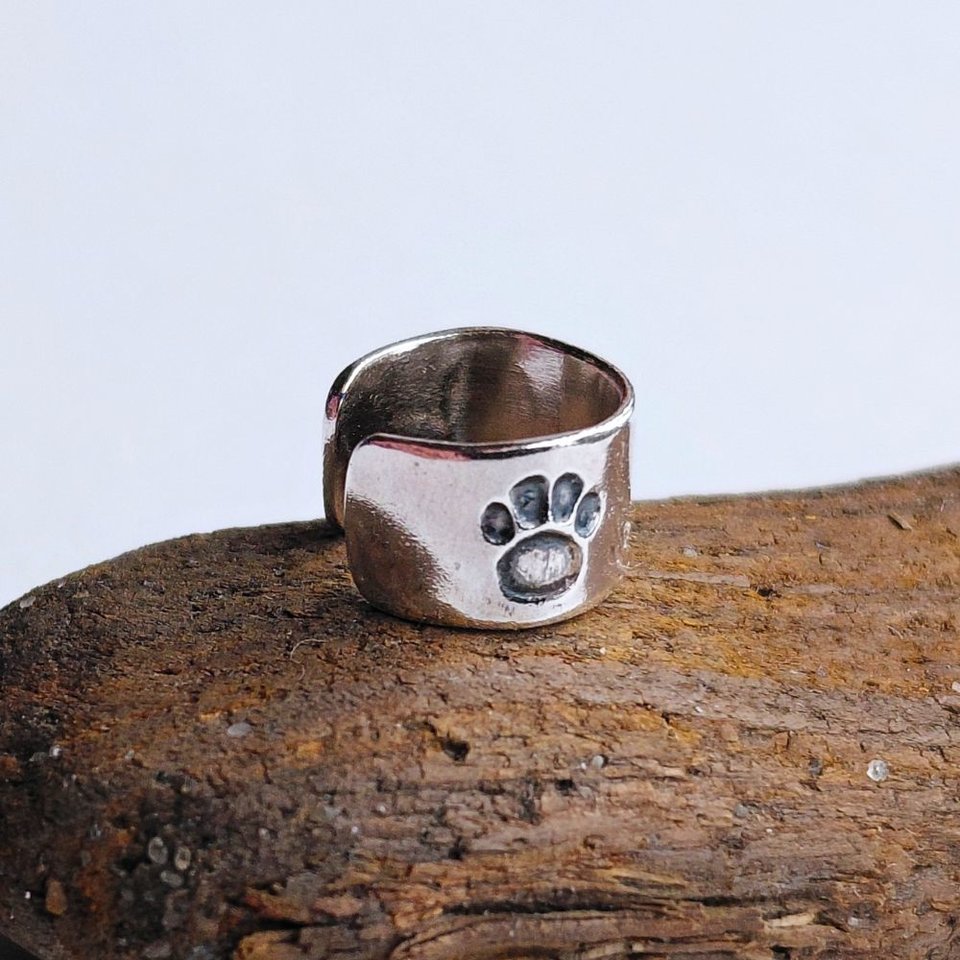 Handcrafted sterling silver paw print helix cuff shown on natural wood, with the hand-stamped paw print clearly visible