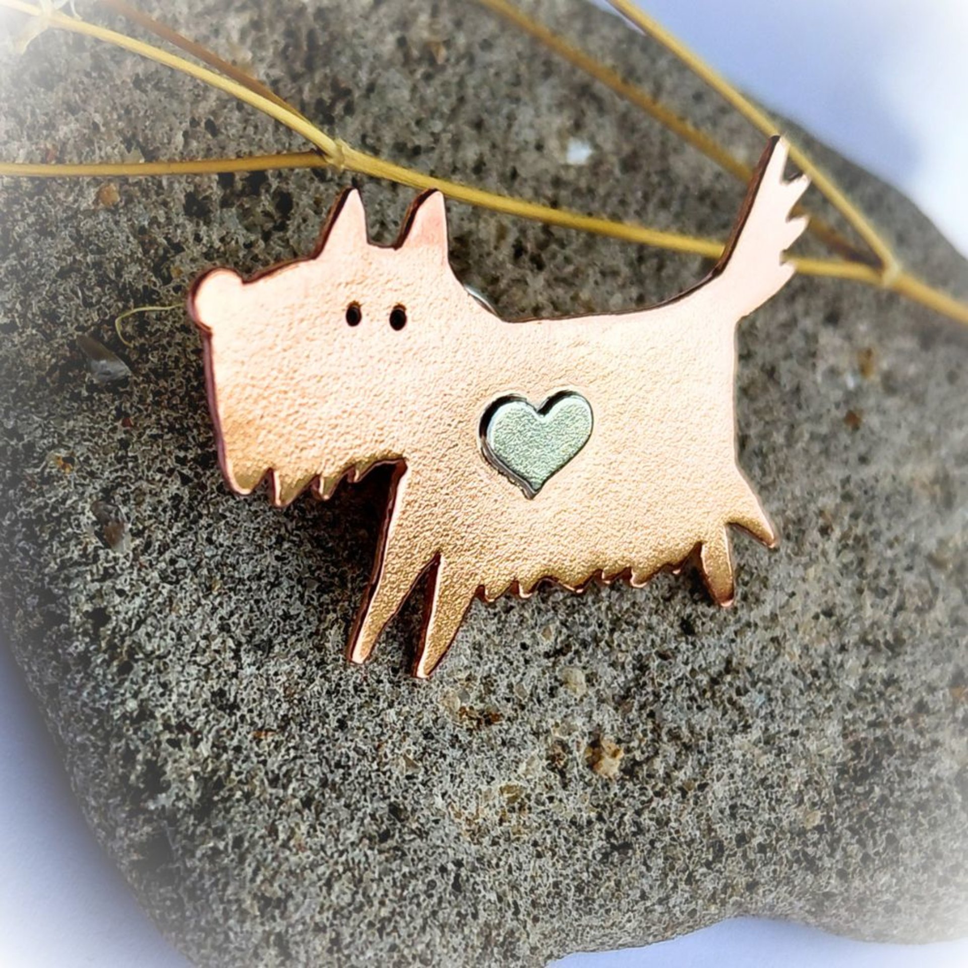 Angled view of the handcrafted copper scruffy terrier dog brooch with a sterling silver heart