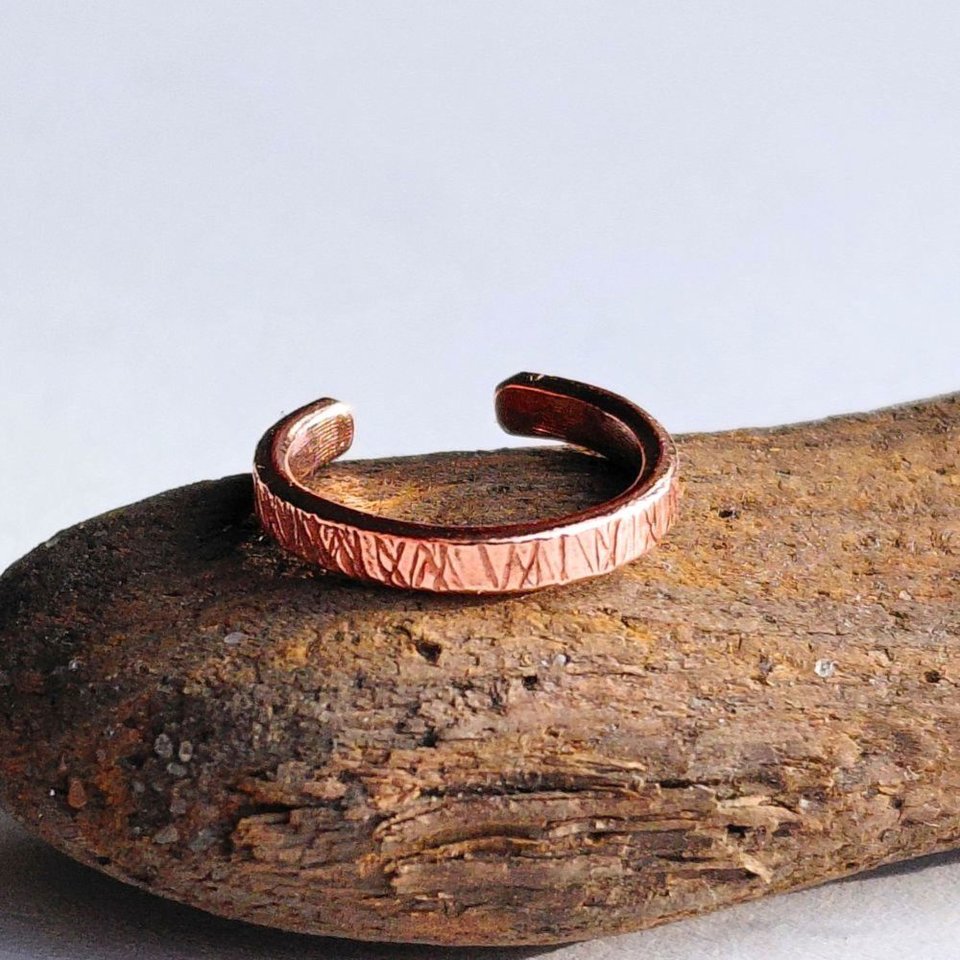 Handcrafted no-piercing copper ear cuff with textured surface, shown on natural driftwood