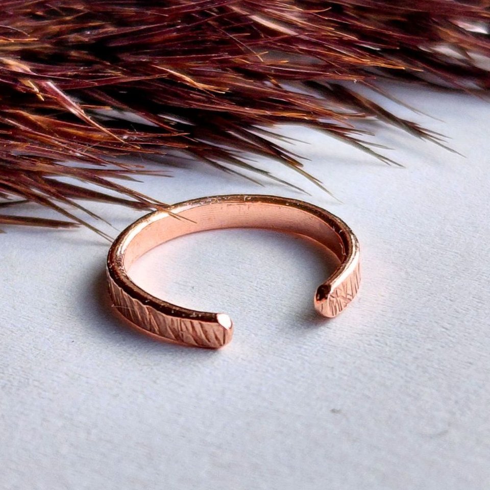 Close-up of a handcrafted copper ear cuff showing its organic hammered texture and open design