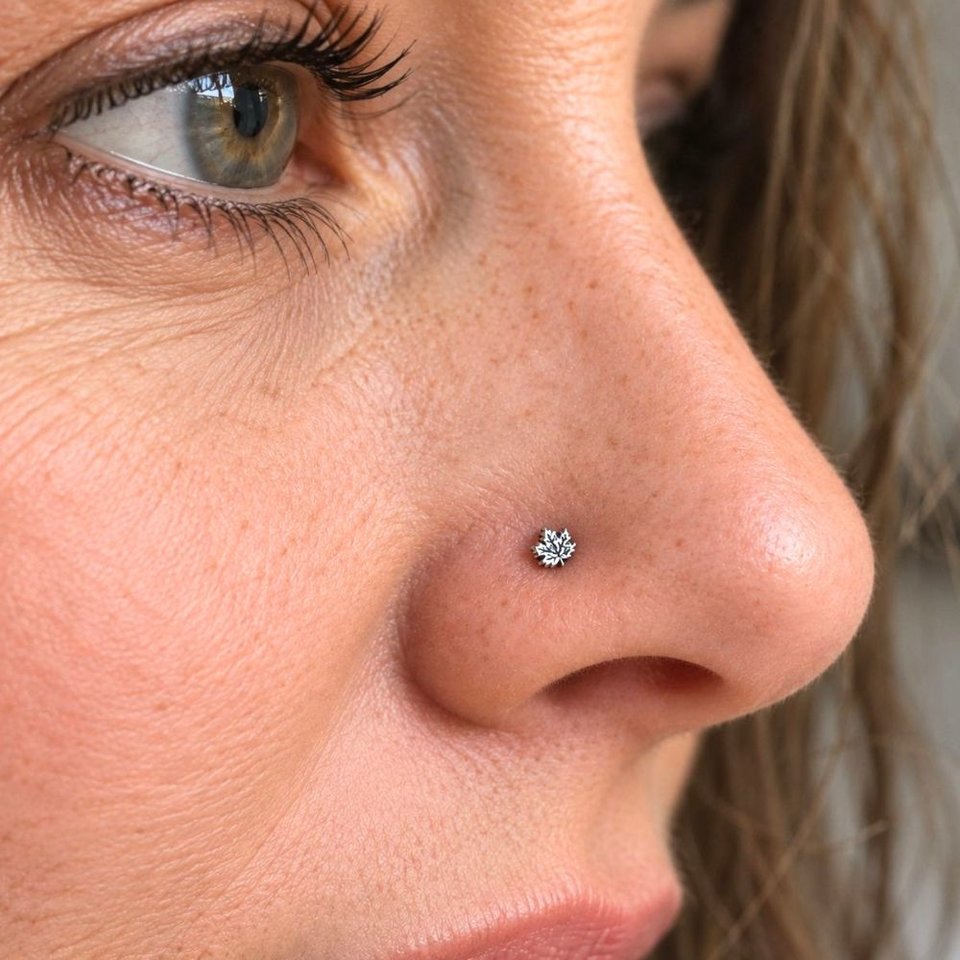 Fine silver maple leaf nose stud worn in a nostril, showing the delicate scale of the design