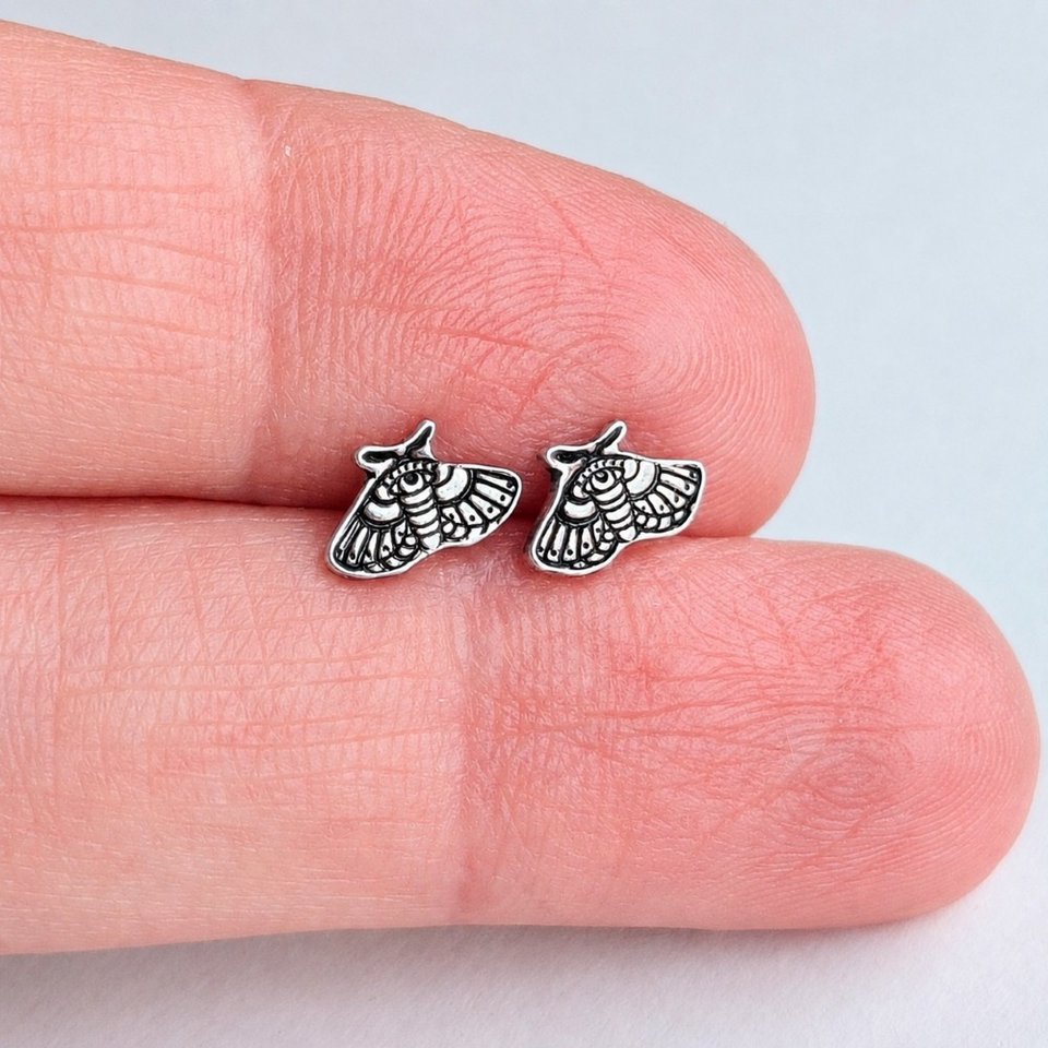 Small sterling silver moth stud earrings held between fingertips to show their size